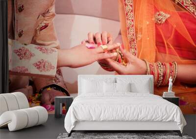 Indian bride putting a wedding engagement ring on finger of groom. Wall mural