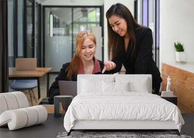 Asian female manager helping, giving advices to young intern at cooperate office  Wall mural