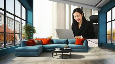 Charming Asian businesswoman in suit working with laptop at modern workplace Wall mural