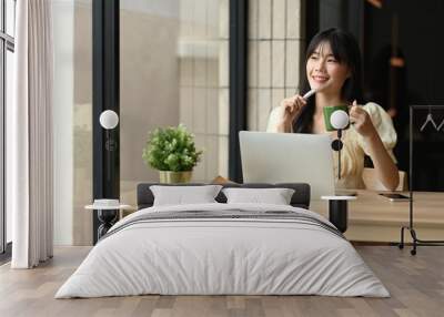 Charming young Asian woman staring out the window of office with a coffee cup in her hand Wall mural