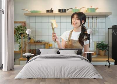 Cheerful young woman holding a slice of toasted bread with tongs in kitchen Wall mural