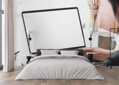 Cropped image of businessman typing on white blank screen computer laptop that putting on working desk with coffee cup, potted plant, pencil holder, books. Concentrated of work concept. Wall mural