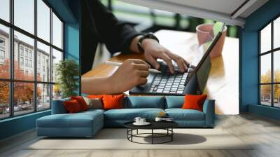 Cropped shot of female hands typing on tablet keyboard on wooden table. Wall mural