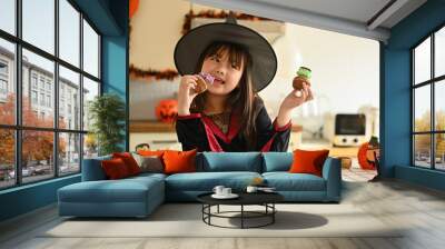 Cute little girl in witch costumes standing behind kitchen table with Halloween desserts Wall mural