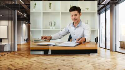 Handsome asian man economist working on financial and marketing project in modern office Wall mural