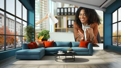 Happy African American businesswoman holding credit card and using laptop for make transactions online Wall mural