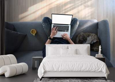 Overhead shot of young man sitting on sofa with his cat in living room and using laptop computer. Wall mural