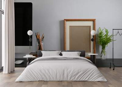 Photo of black working desk along with black blank screen computer monitor, books, notebook, pencil holder, picture frame, potted plant putting together on it with white cement wall as background. Wall mural