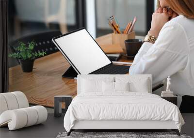 Photo of young beautiful woman working as secretary sitting and concentrated on white blank screen computer tablet with keyboard case at the modern wooden table with orderly office as background. Wall mural