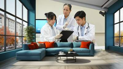 Senior female scientist and young laboratory assistants analyzing and summarising information for scientific report Wall mural