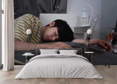 Tired young asian man sleeping on bed near computer laptop. Wall mural