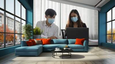 Young asian business people in protective mask discussing business idea and working together in office. Wall mural