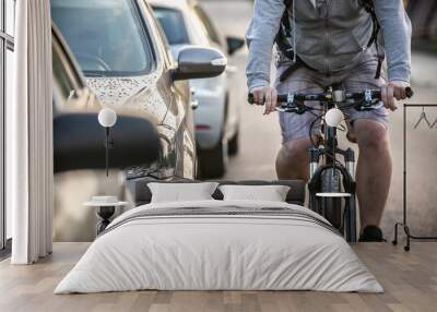 An unidentified man riding a bicycle passing cars on the road. Wall mural