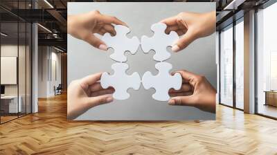 Four hands holding puzzle pieces together, symbolizing teamwork and collaboration on a light gray background. Wall mural