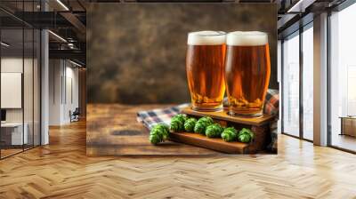 Two glasses of golden beer with frothy tops, sitting on a wooden table alongside fresh hops, creating a rustic atmosphere. Wall mural