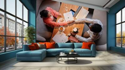 Above view of two successful white collar workers handshaking over table with mobile gadgets, financial documents, coffee and snack Wall mural