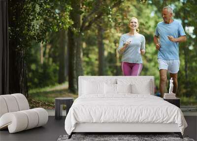 Active and healthy aged couple running in natural environment on summer morning Wall mural