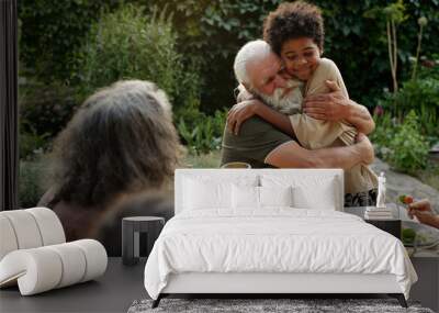 Affectionate senior man embracing his African American grandson while sitting by dinner table served with healthy and tasty homemade food Wall mural