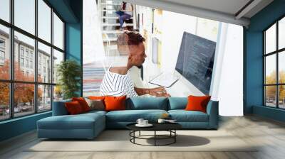 African-american it-specialist looking attentively at coded data on computer screen while working in office Wall mural