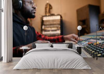 African American music producer working in record studio adjusting mixing console settings, selective focus shot Wall mural