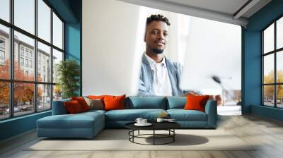 African-american young it-manager looking at you while sitting between two monitors and working with software Wall mural