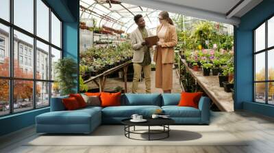 African young landscape designer discussing list of plants together with woman standing in flower shop Wall mural