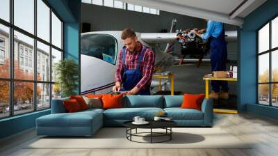 Airplane service crew working on preflight maintenance:  two young mechanics, man and woman, repairing jet plane in hangar Wall mural