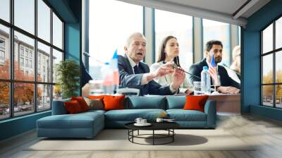 Annoyed emotional handsome senior diplomat in suit making public announcement into microphone and gesturing while saying his opinion at Commonwealth meeting Wall mural