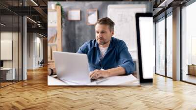 Architect sitting in front of laptop, looking through data and making sketch Wall mural