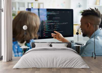 Busy young interracial colleagues analyzing computer code on computer: African man pointing at monitor and asking coworker in office Wall mural