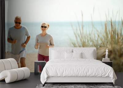 Cheerful and active couple of retired spouses jogging in the morning on the beach Wall mural