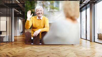 Cheerful and friendly mature man waving hand to his neighbour while standing by fence Wall mural