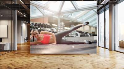 Cheerful and healthy young woman lying on side and lifting her upper leg during workout Wall mural