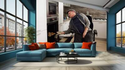 Contemporary man with disability taking homemade cookies out of electric oven in kitchen environment Wall mural