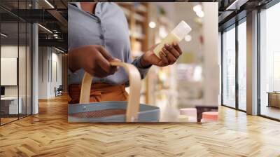 Cropped shot of young African American woman in casualwear holding plastic bottle with cosmetic product and shopping baskest Wall mural