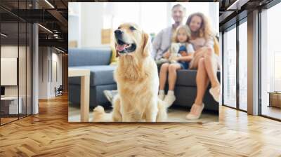 Cute fluffy labrador pet sitting in living-room with family of three on background Wall mural