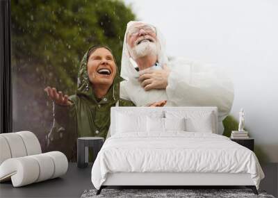 Ecstatic female and her husband in raincoats enjoying rainy weather in natural environment Wall mural