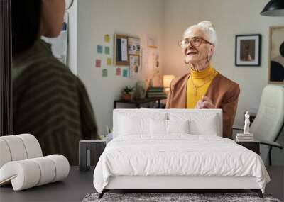 Elderly businesswoman conversing with coworker in office filled with charts and posters. Engaging in detailed discussion about business strategies and developments Wall mural