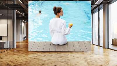 Girl in white bathrobe enjoying drink by swimming pool at resort Wall mural