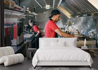 Gloved man in uniform putting fast food on electric stove for baking or frying Wall mural