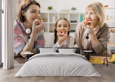 Group of hungry females eating homemade sandwiches with cheese and cherry tomatoes in the kitchen Wall mural