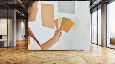 Hand of young woman with palette of color swatches choosing one for walls of living room or bedroom during renovation of new apartment Wall mural