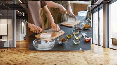 Hands of two young women cutting hard soap mass into cubes on wooden boards Wall mural