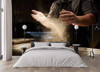 hands of young male chef sprinkling flour on dough flatbread before kneading it on table in the kitchen while preparing pizza Wall mural