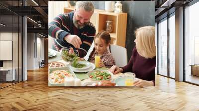 Happy mature man giving salad to his adorable granddaughter by festive table Wall mural