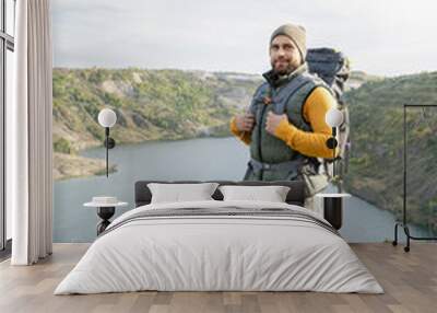 Happy young bearded tourist with backpack standing on top of mountain Wall mural