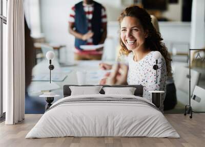 Happy young businesswoman sitting at desk and communicating with her colleagues during a meeting Wall mural