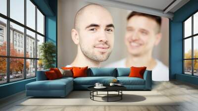 Happy young man with bald head looking at camera with his partner on background Wall mural