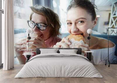 Hungry young women eating tasty fast food during lunch break in cafe Wall mural