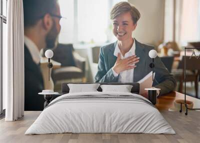 Laughing businesswoman with papers talking to her colleague during meeting in cafe Wall mural